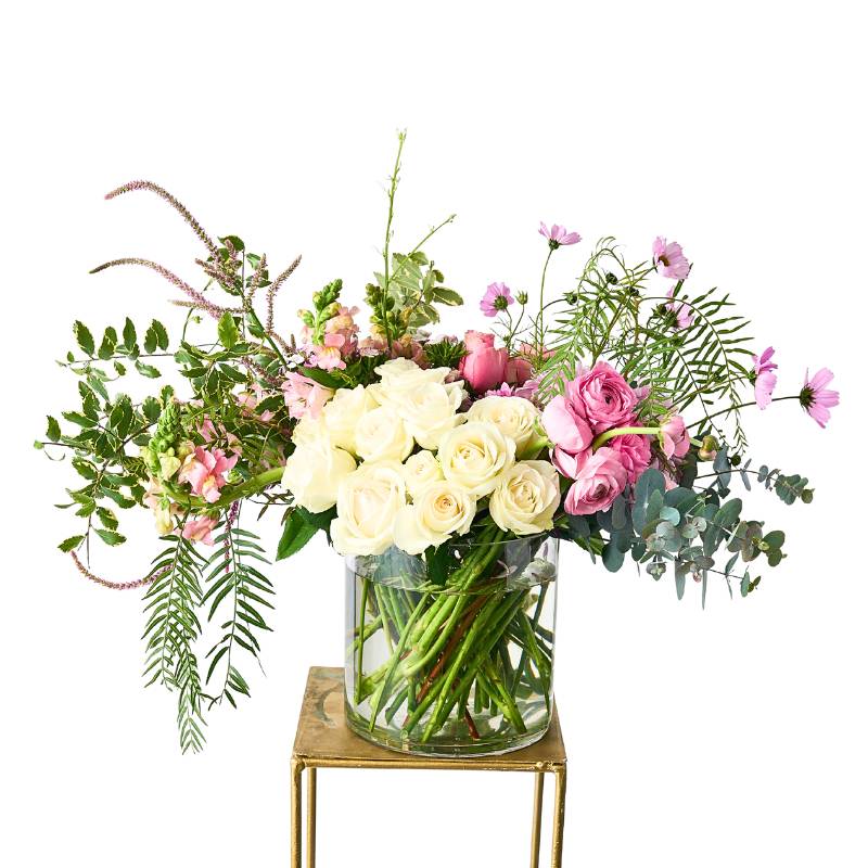 Large Arrangement of flowers in a clear vase on a small wooden table with a white background