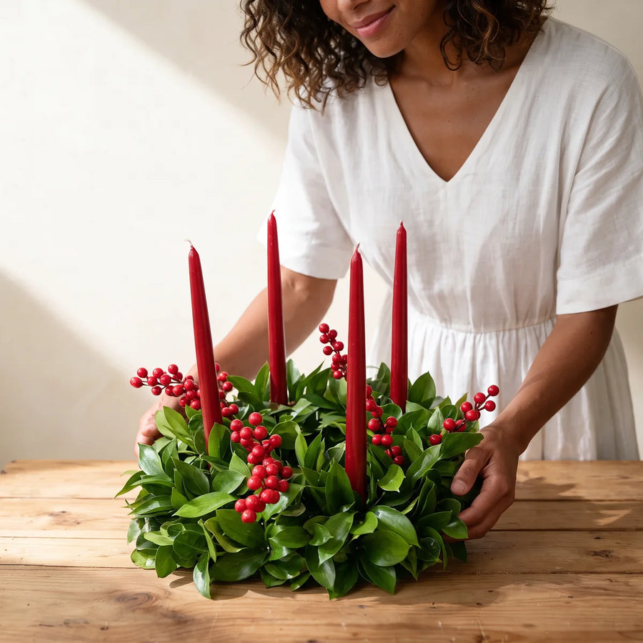 Woman in a white linen dress setting a red berry wreath with red candles on a wooden table, Fabulous Flowers South Africa