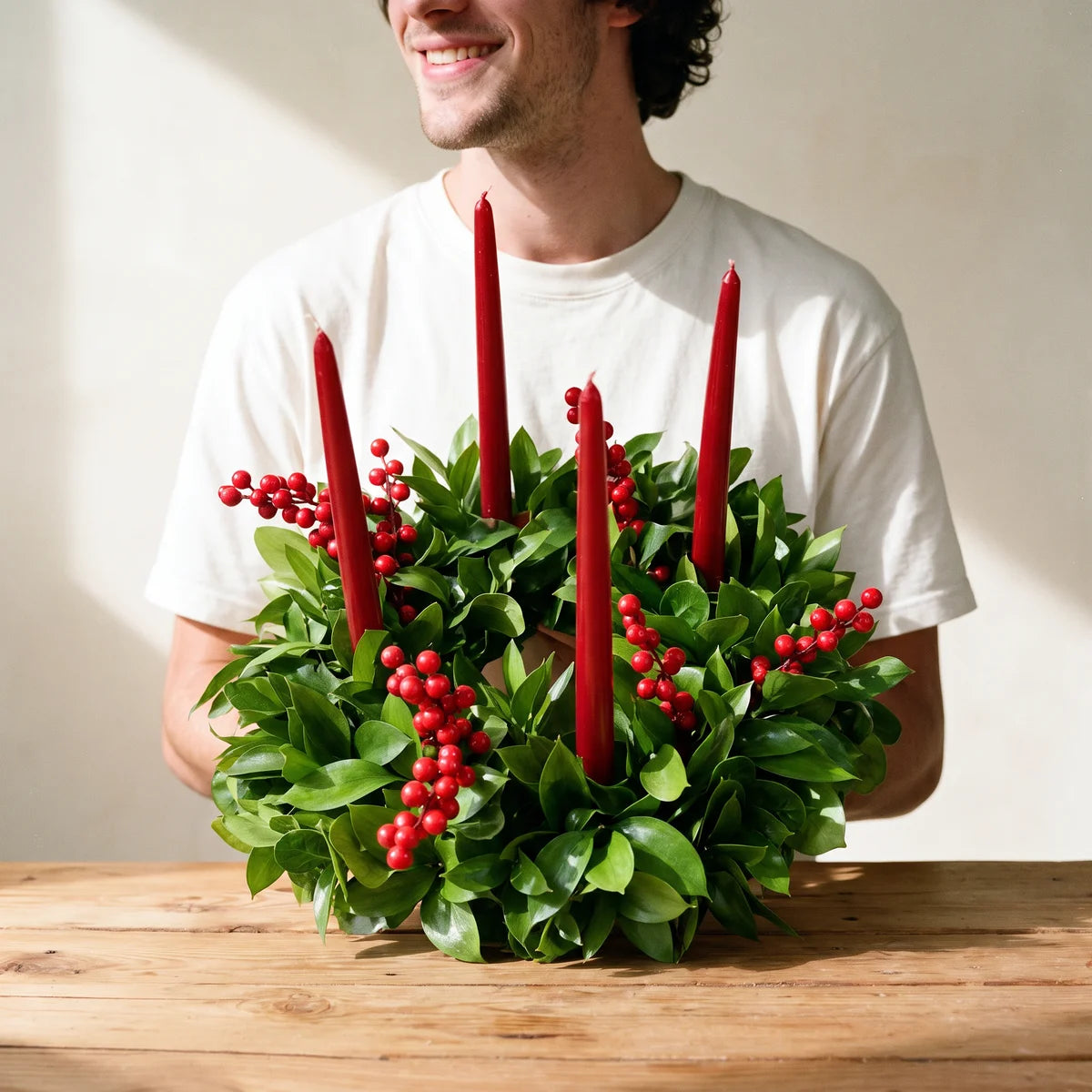 Man in a white t-shirt holding a green wreath with red candles and red berries, Fabulous Flowers South Africa