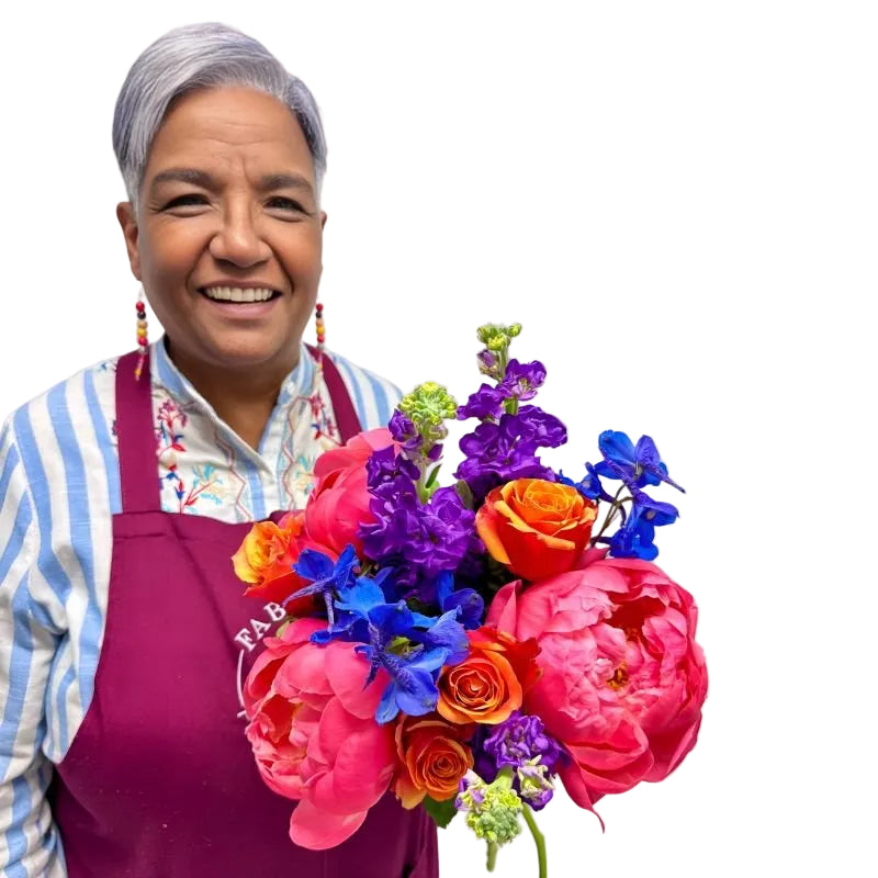 Electric Bloom bouquet with vibrant pink peonies, orange roses, and blue delphiniums held by a smiling florist in apron.