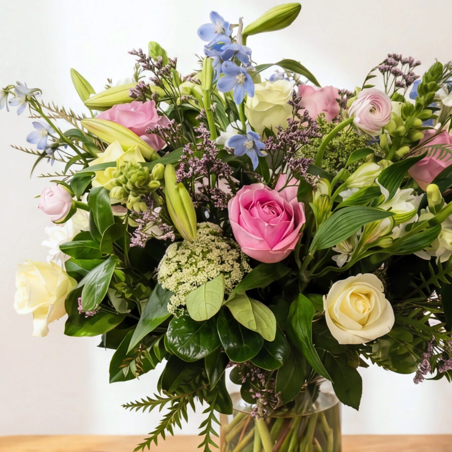 Close view of English Garden vase with pink roses, blush ranunculus, lilac limonium, blue delphiniums and lilies in bud