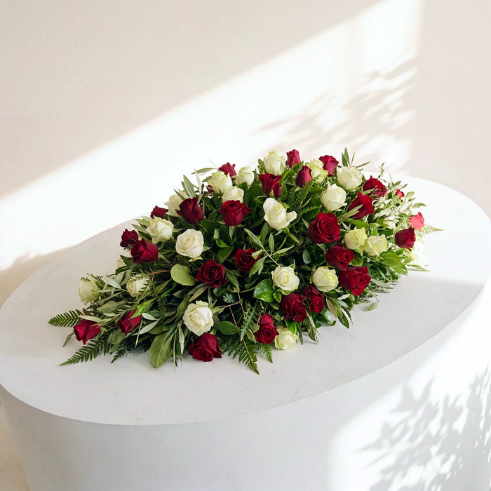 Evermore coffin flowers, a medium casket spray of red and white roses with olive and fern on a white plinth