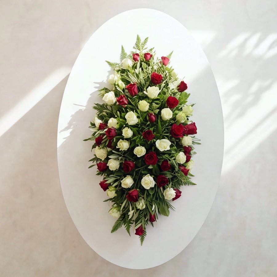 Top down view of the Evermore casket spray showing red and white roses among garden greenery
