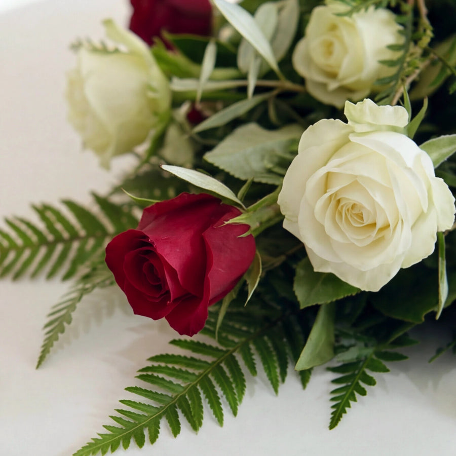 Close up of a deep red rose and ivory roses with fern in the Evermore coffin spray