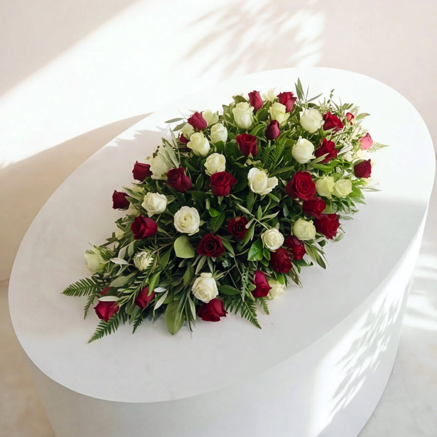 The Evermore medium coffin spray of red and white roses laid across a white casket
