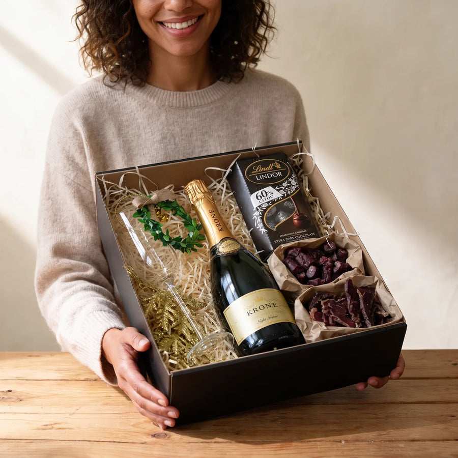 Smiling woman holding an open black gift box of sparkling wine, flutes, chocolate and biltong, Fabulous Flowers South Africa
