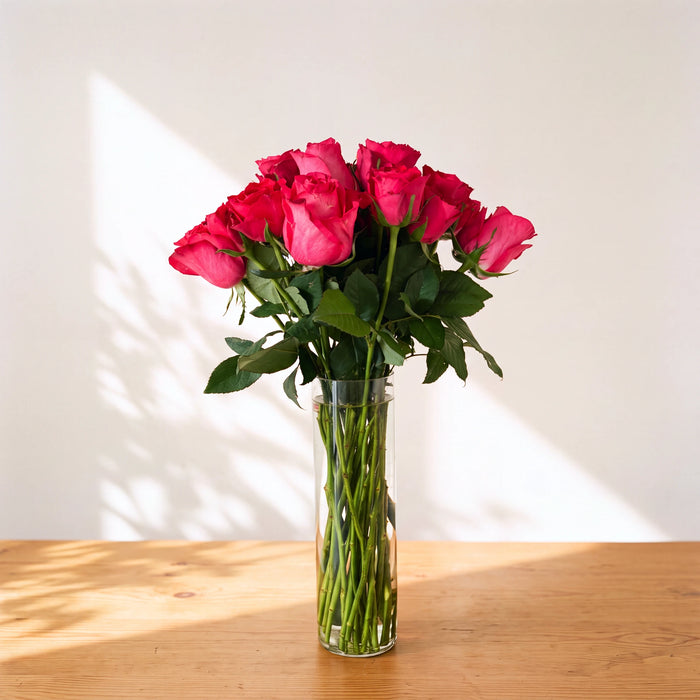 Small Fandango vase of hot pink cerise roses in a clear glass cylinder on a wooden table