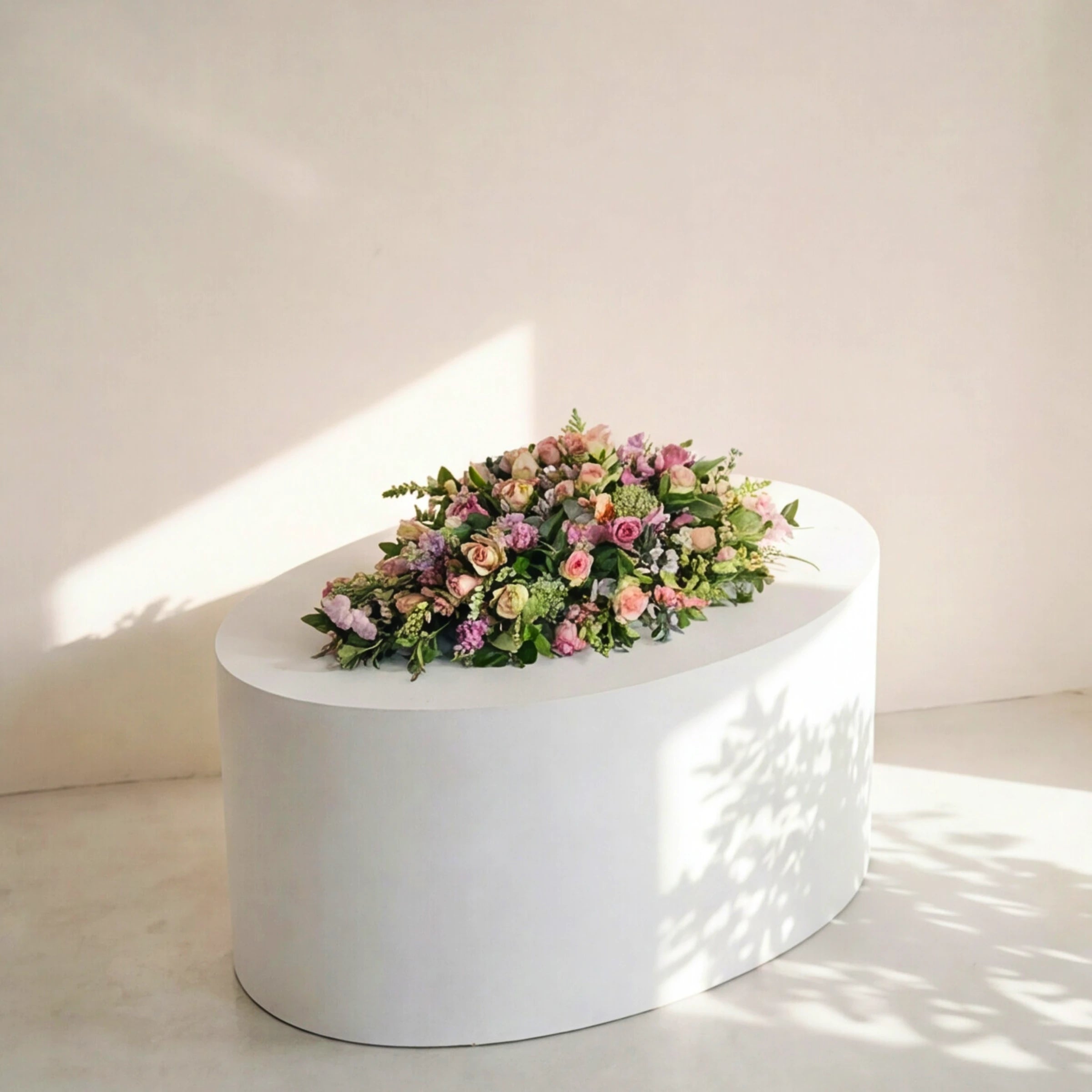 The Forever Loved coffin spray on a white oval plinth in soft daylight