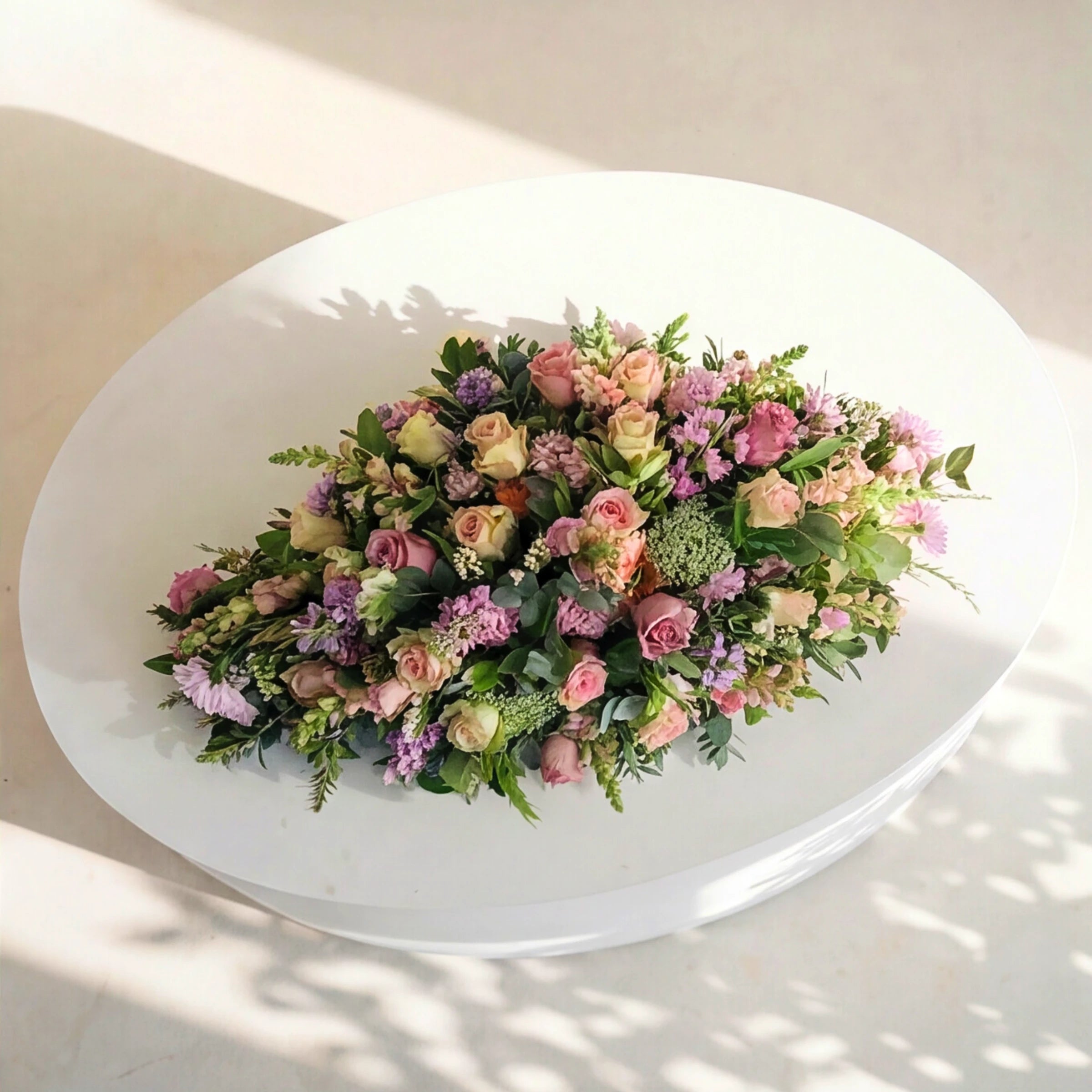 Top-down view of the Forever Loved coffin spray, a teardrop of pink and lilac blooms