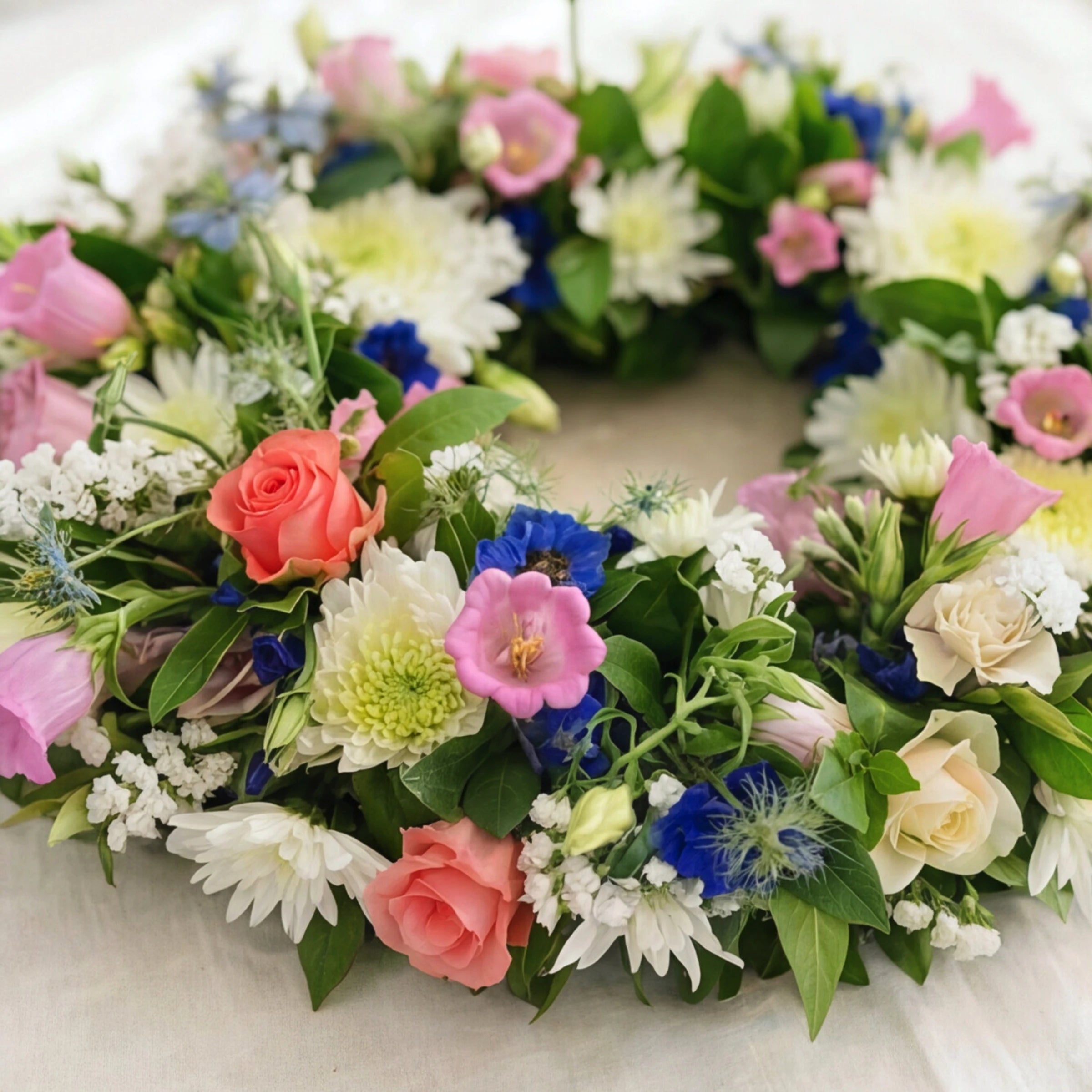 Close up of the Forget Me Not wreath with a coral rose, pink Canterbury bells and deep blue delphinium