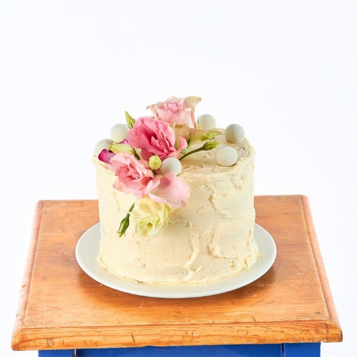 Elegant vanilla buttercream cake adorned with pink roses and peonies, perfect for a garden tea party, presented on a rustic wooden table.