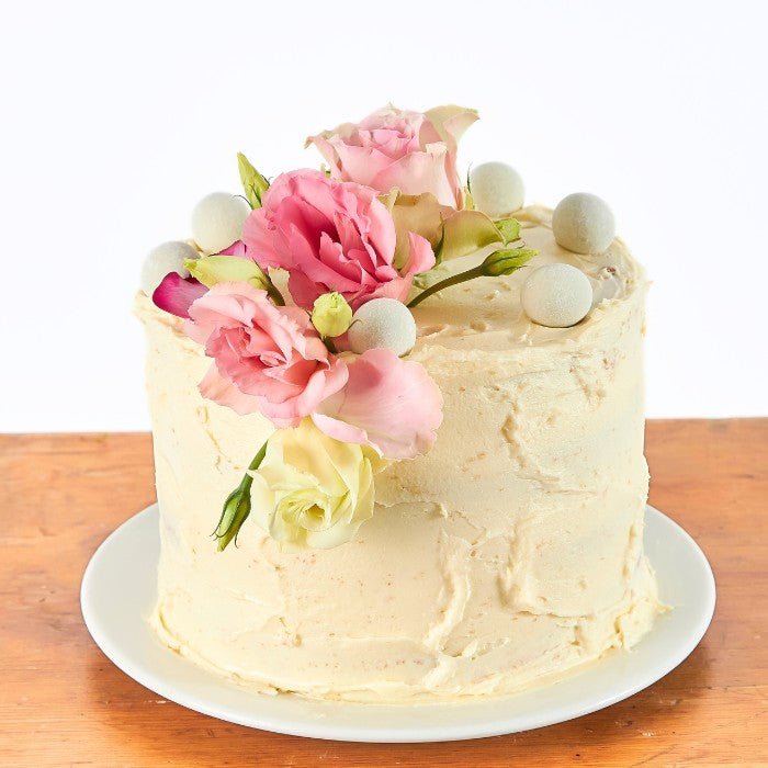 Close-up of a buttercream-frosted cake decorated with fresh flowers and sugar pearls, ideal for celebrations, displayed on a classic white plate.