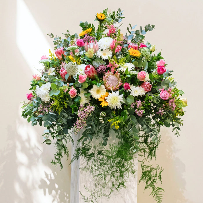 Garden of Grace funeral service flowers, a large standing tribute of proteas, roses and gerberas on a plinth.