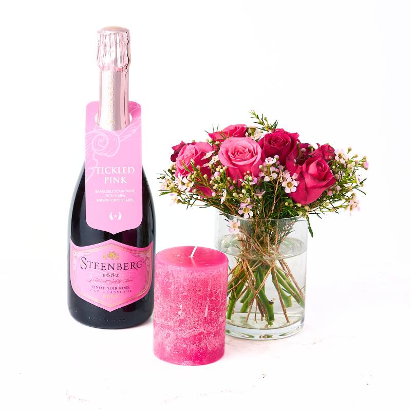 Bottle of pink Steenberg wine, pink candle, and bouquet of pink flowers on a white background