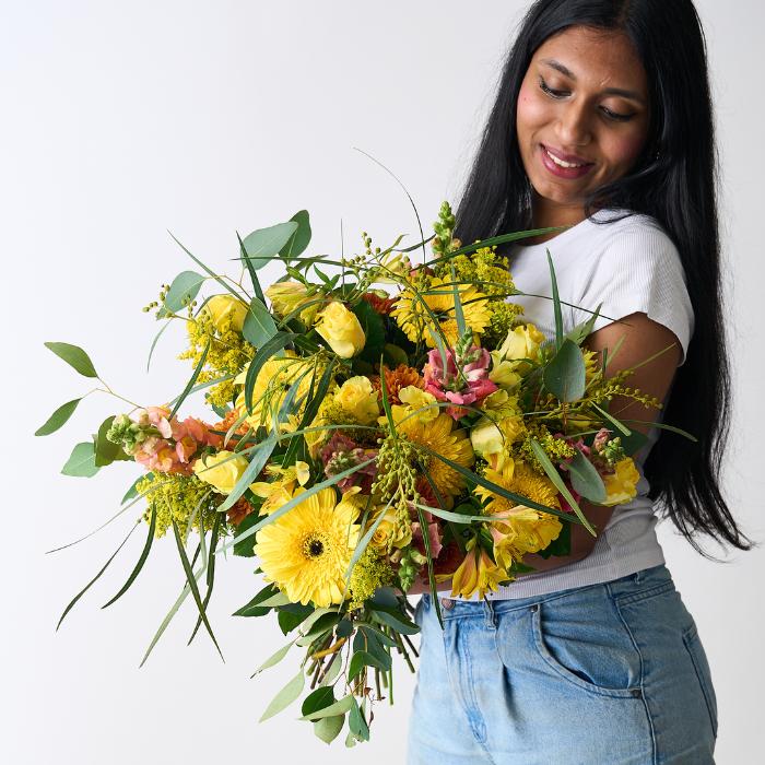 Woman holding a vibrant Golden Hues Bouquet from Fabulous Flowers, featuring yellow gerberas, roses, snapdragons, and lush greenery.