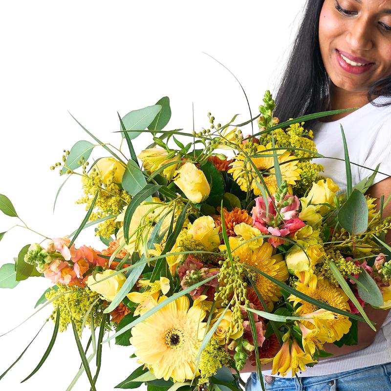 Close up of a orange and yellow bouquet as a woman smiles holding it