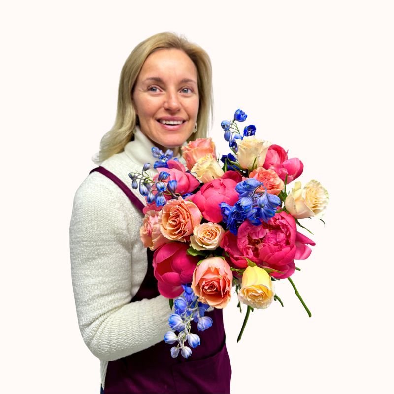 Florist presenting the Heart & Bloom bouquet with joyful expression, holding mixed peonies, roses and delphiniums.