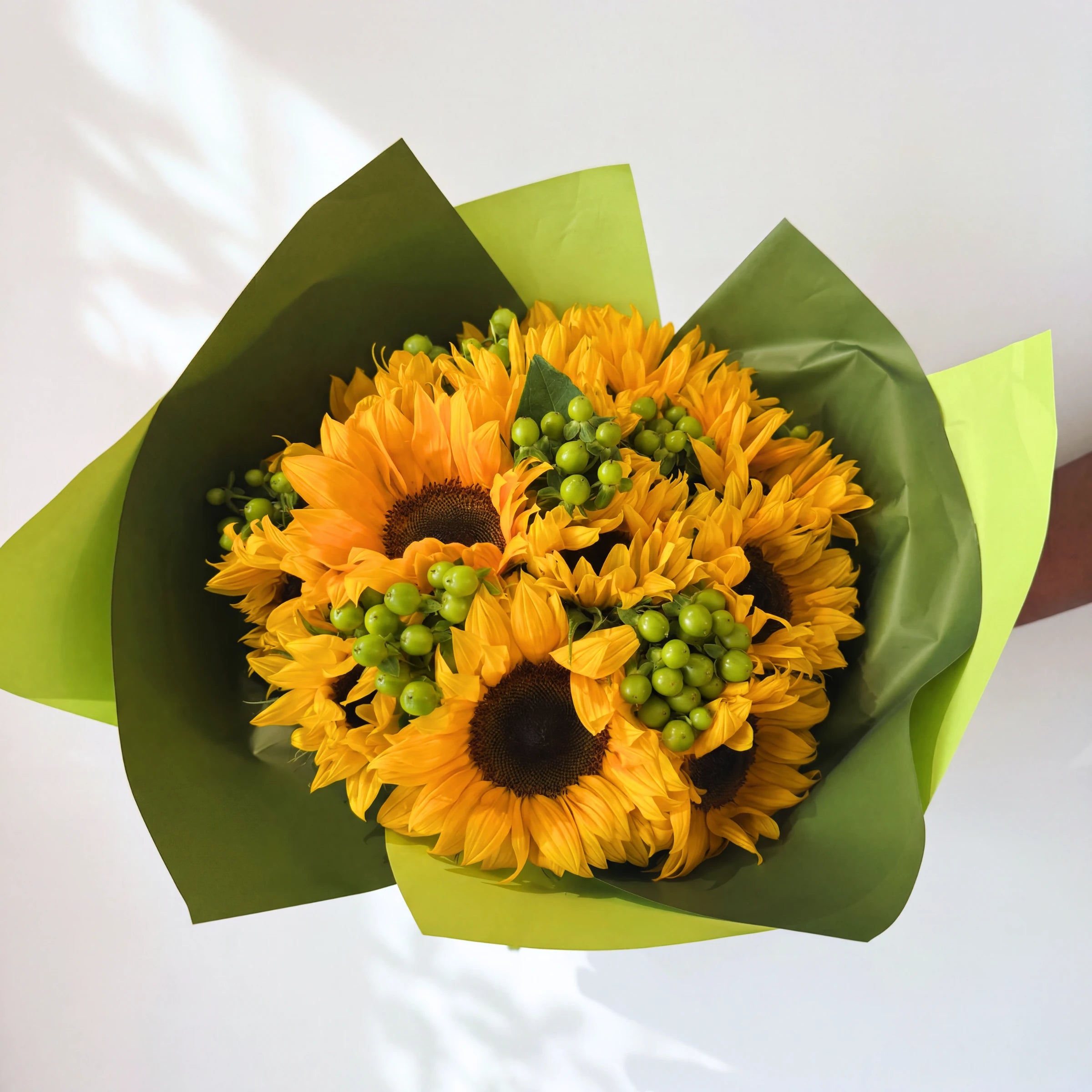 Top-down view of the Here Comes the Sun bunch, sunflowers and green berries in green wrap