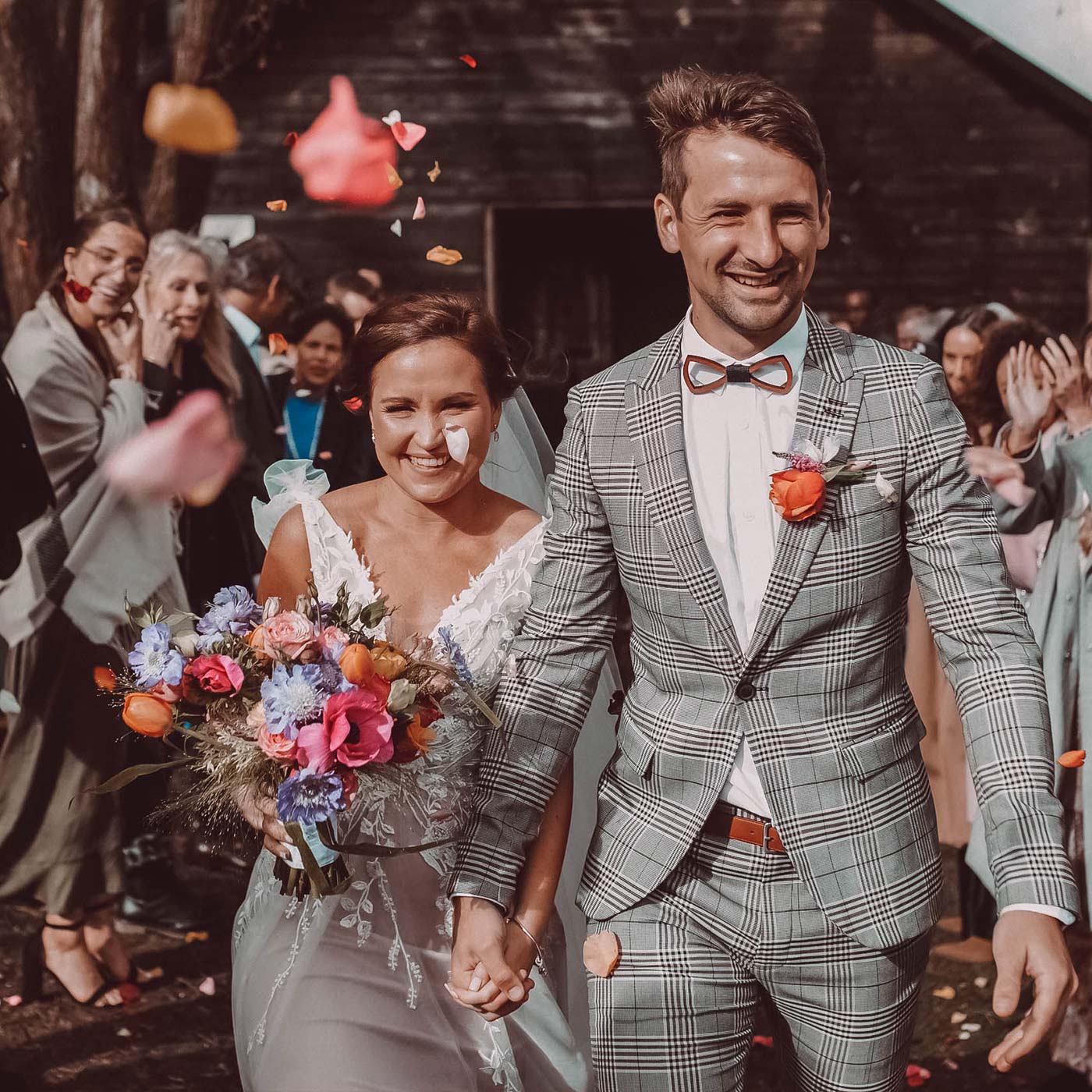 Bride Jodi and groom Wesley exit their wedding ceremony holding hands, surrounded by guests tossing flower petals. Jodi holds a vibrant bouquet. Weddings. Fabulous Flowers and Gifts.