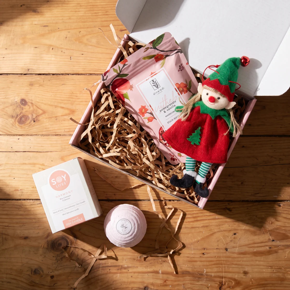 Pink gift box of bath salts and a felt elf ornament seen from above, with a soy candle box and a pink bath bomb beside it on a wooden table, Fabulous Flowers South Africa