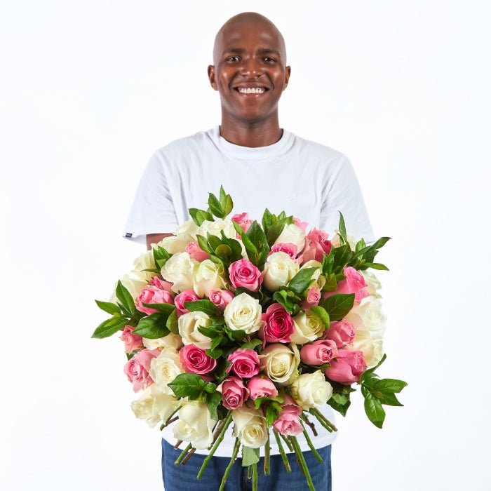 Kindness in Bloom bouquet with 55–60 white and pink roses, hand-held by a smiling person in a white t-shirt.
