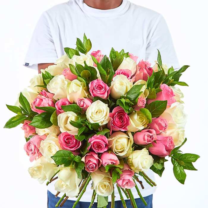Person holding Kindness in Bloom bouquet featuring blush pink roses, creamy white roses and fresh green foliage