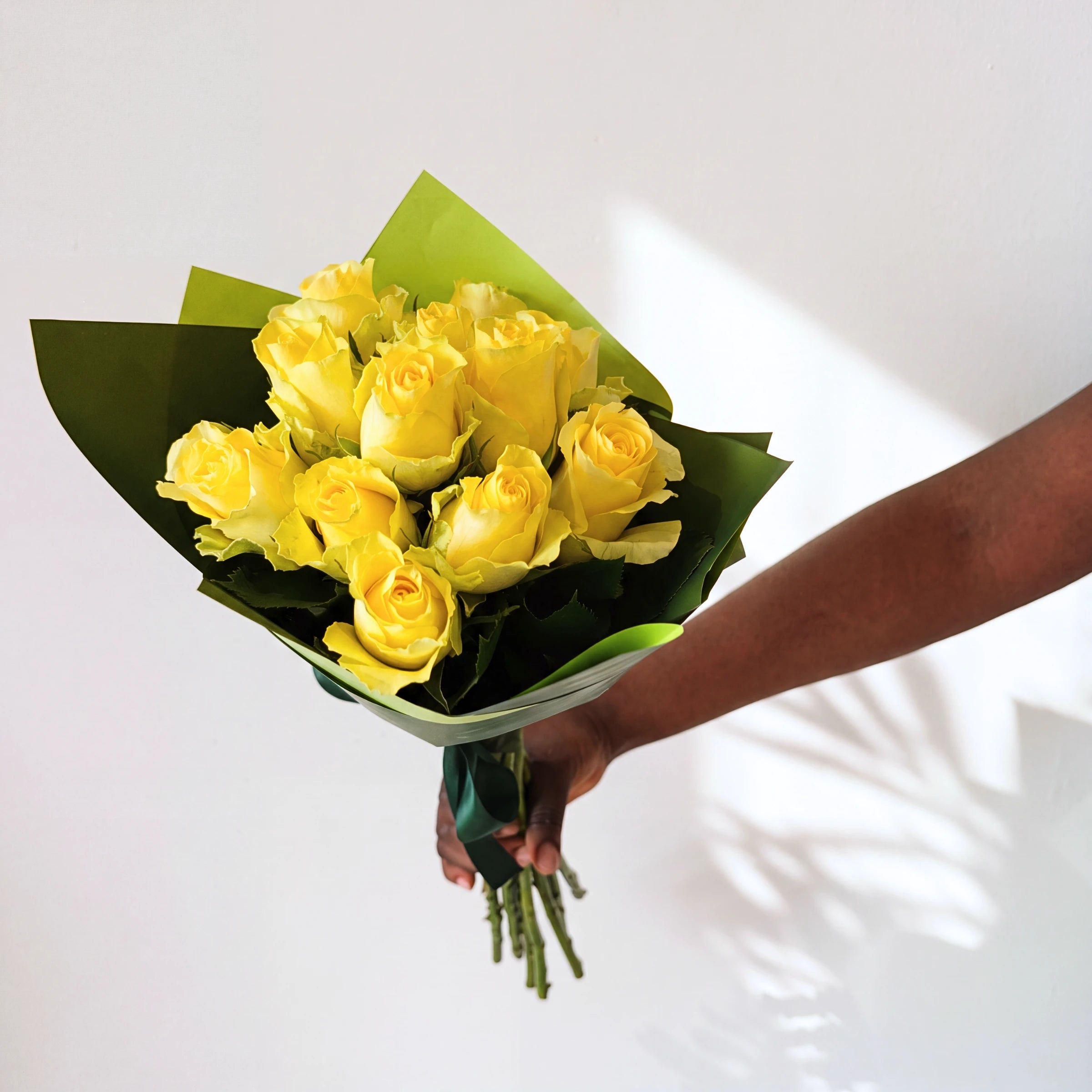 A dozen yellow roses in the Lemon Drop bouquet, green-wrapped and held up in soft window light