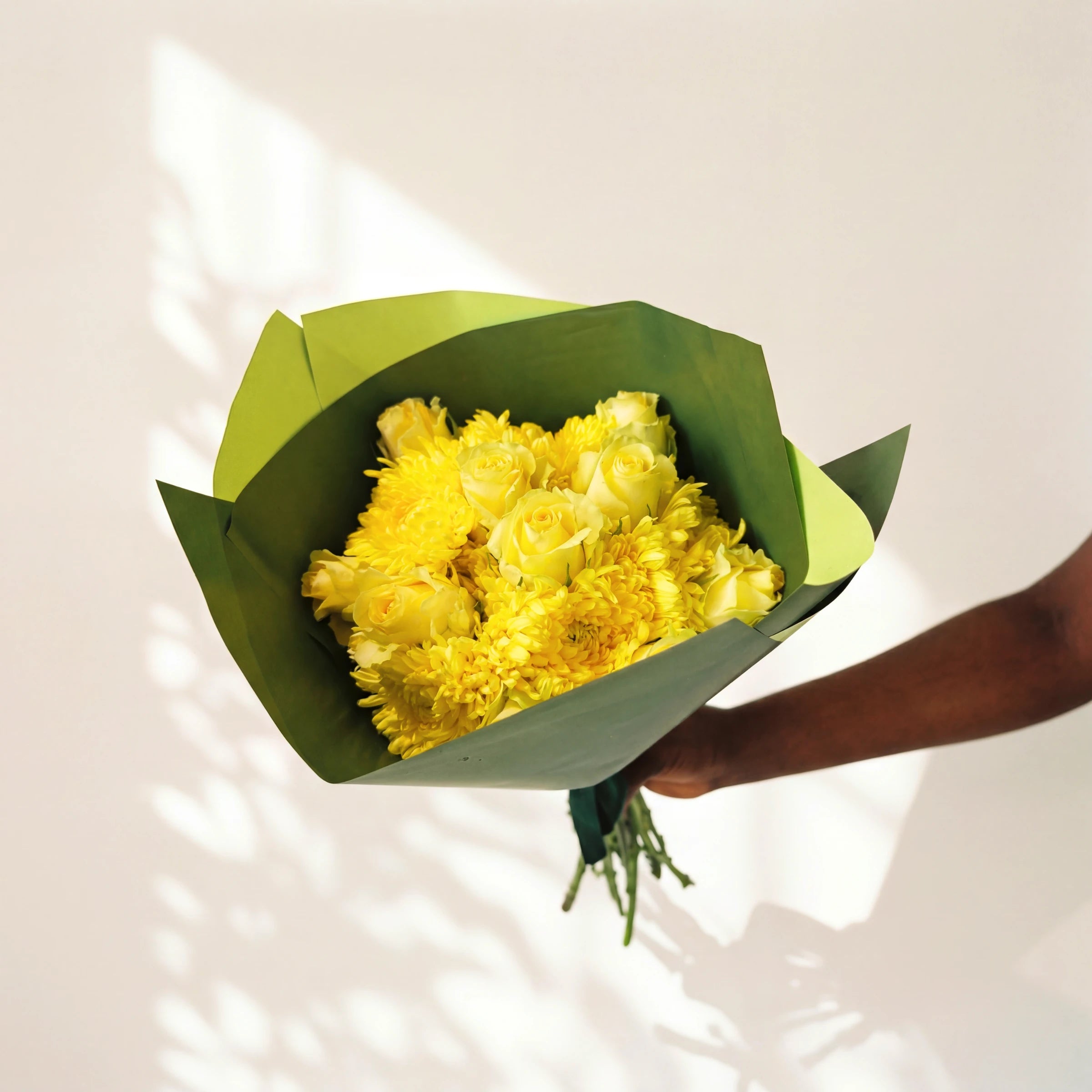 Limoncello yellow roses bouquet held against a sunlit wall, yellow roses and chrysanthemums in green wrap