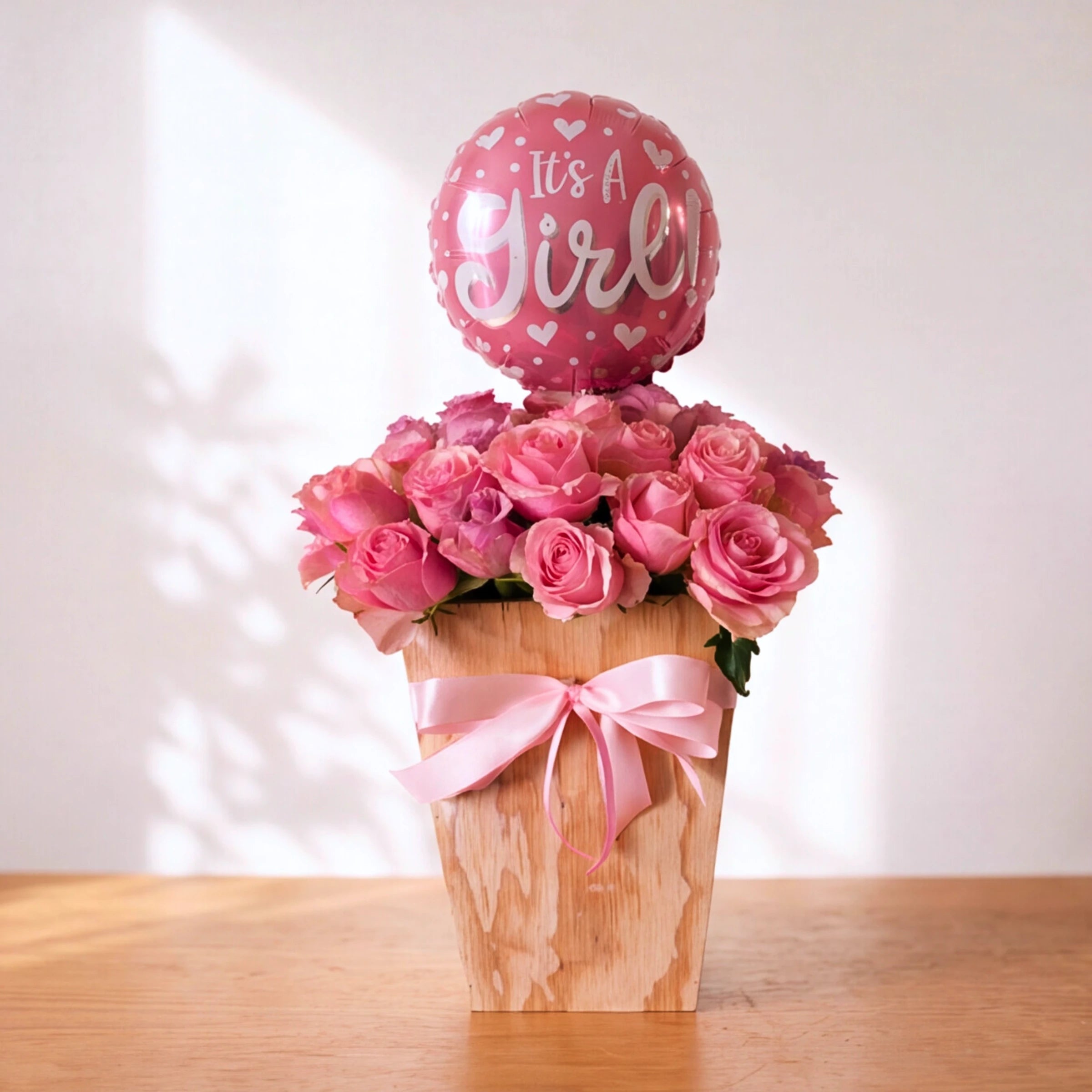 Little Sweetheart It's a Girl pink rose box with pink bow and It's a Girl balloon on a wooden table