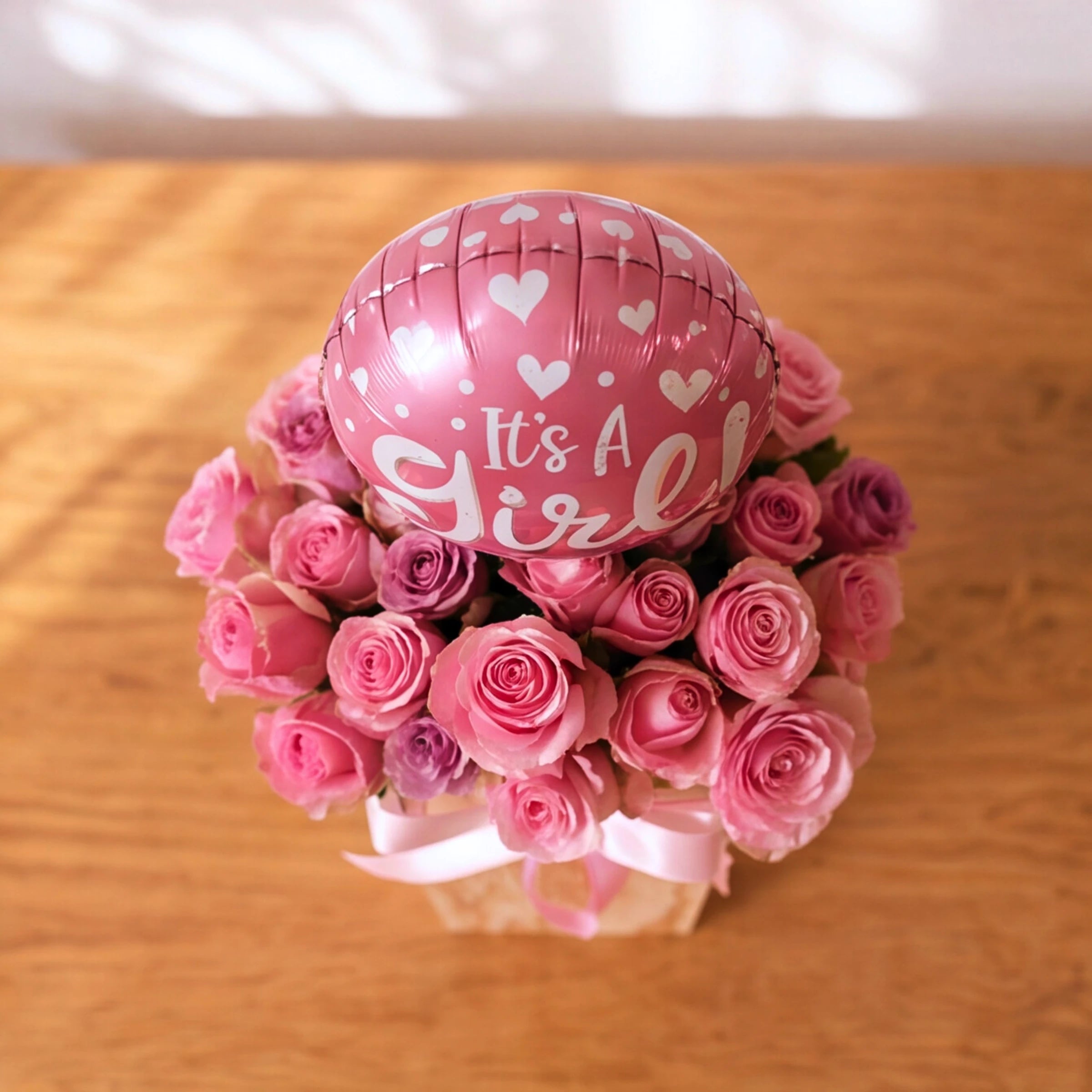 Overhead view of pink and lilac roses with an It's a Girl balloon in the Little Sweetheart baby girl box