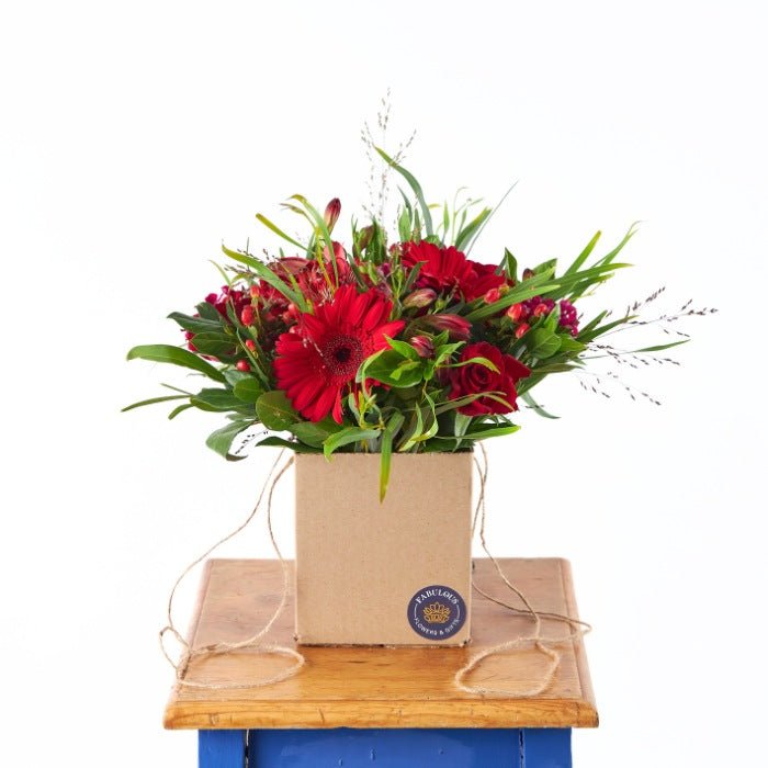 Love's Charm Posy by Fabulous Flowers & Gifts featuring red roses and gerberas in a natural gift box with lush greenery.