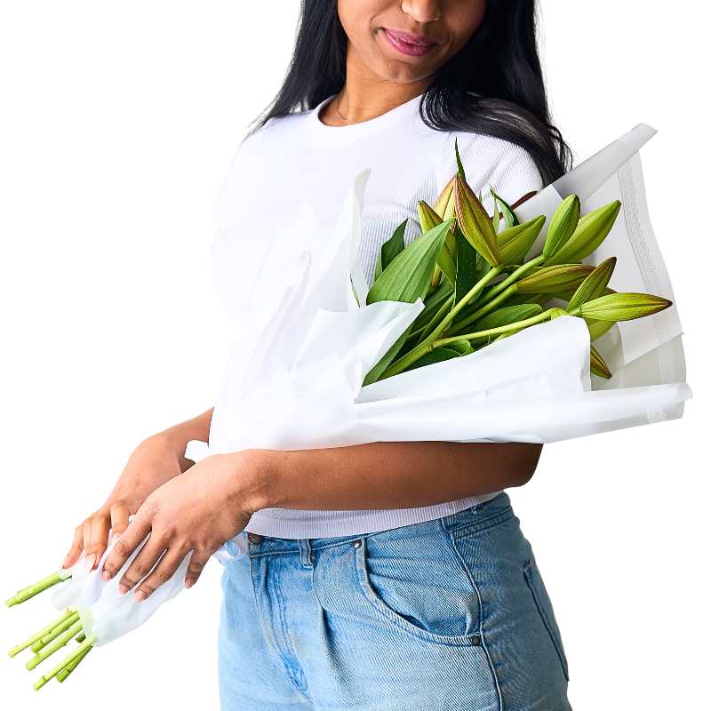 Woman holding a fresh bundle of long-stem white lilies against a white top and jeans