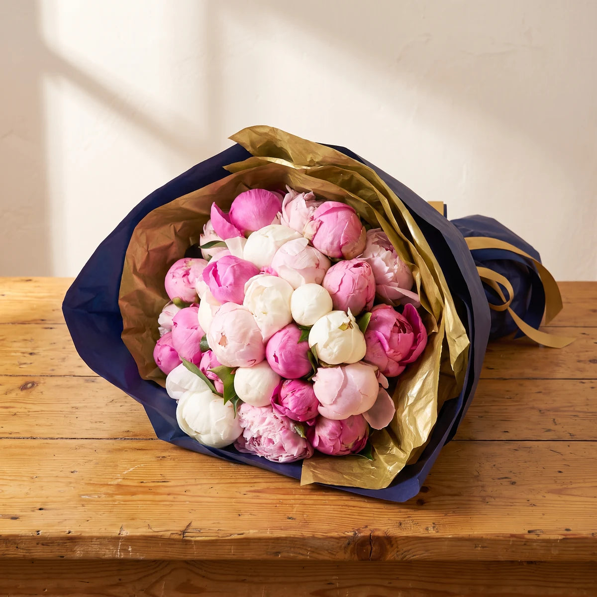 Luxury peony bouquet of blush pink, white and hot pink peonies wrapped in gold and navy paper on a rustic pine table, Fabulous Flowers Cape Town