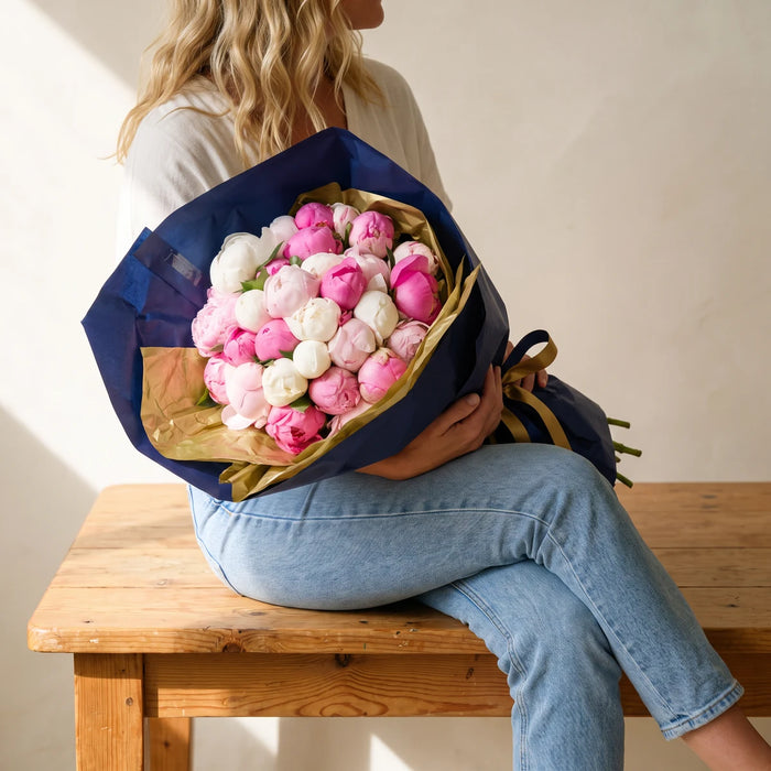 Blonde woman seated with a luxury peony bouquet of pink and white peonies in her lap