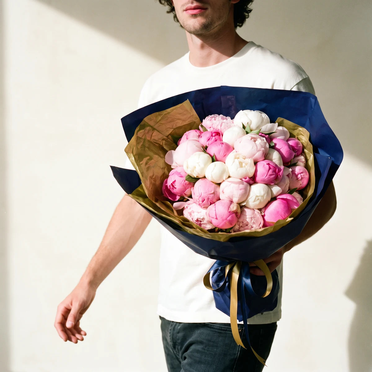 Man carrying a luxury peony bouquet as a gift, pink and white peonies in gold and navy wrapping