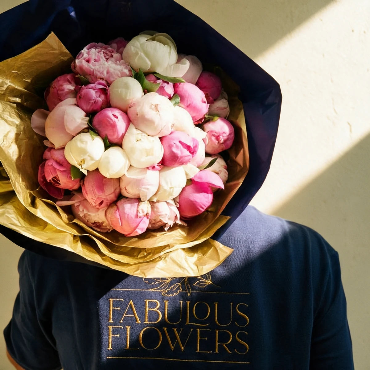 Fabulous Flowers florist in a navy branded polo holding a luxury peony bouquet over his shoulder