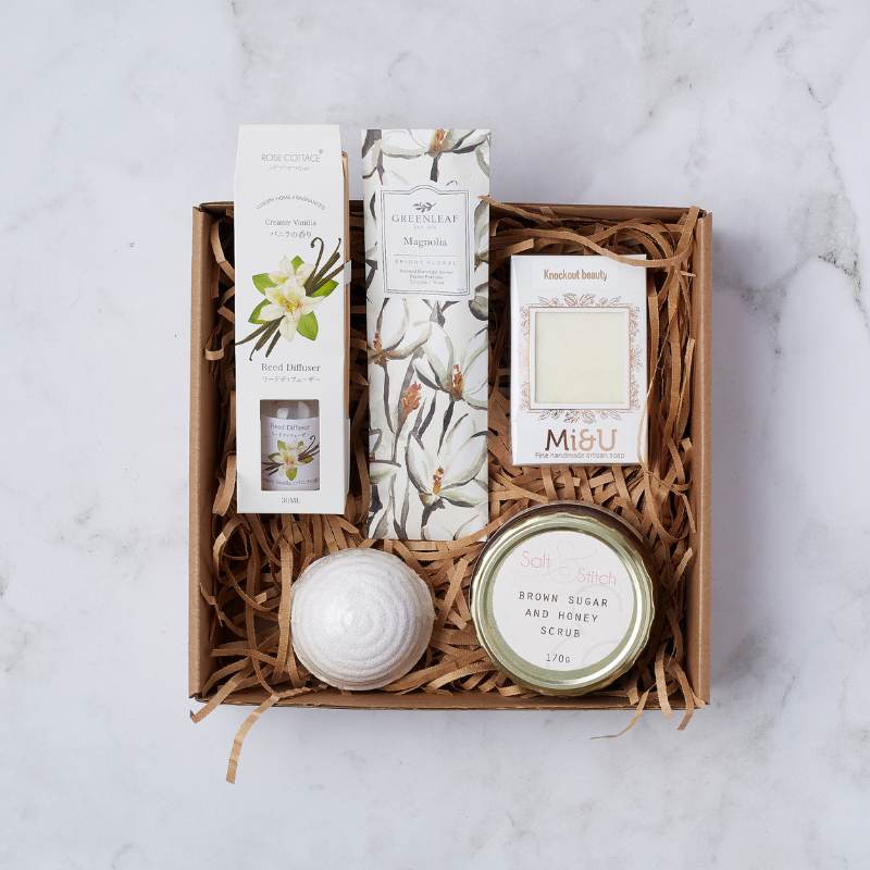 Magnolia Spa Gift Box featuring creamy vanilla reed diffuser, magnolia-scented candle, bath bomb, and brown sugar honey scrub.