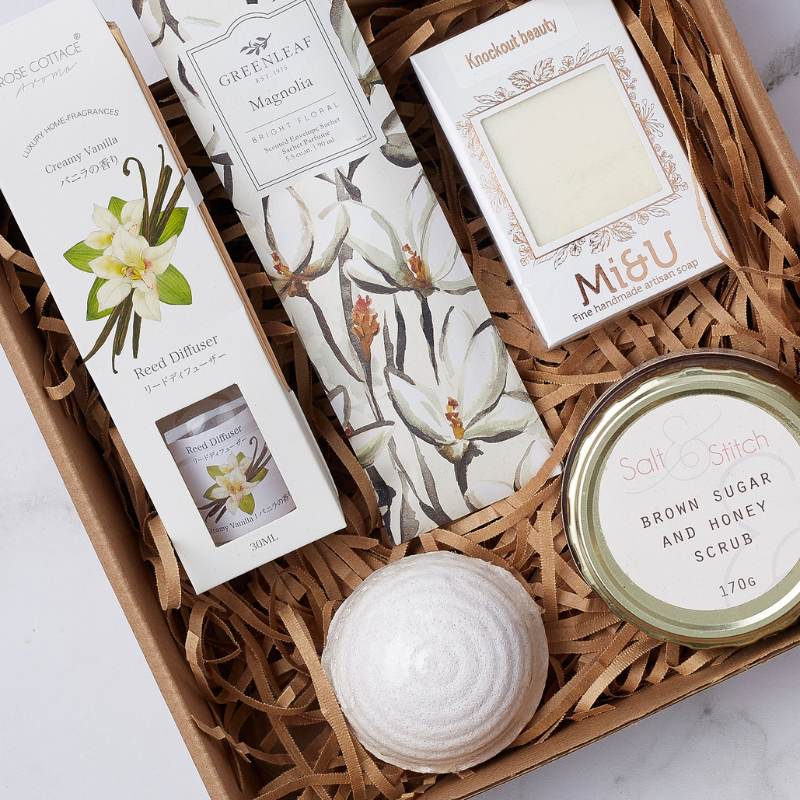 Close-up of Magnolia Spa Gift Box with vanilla reed diffuser, magnolia candle, bath bomb, honey scrub, and artisan soap.