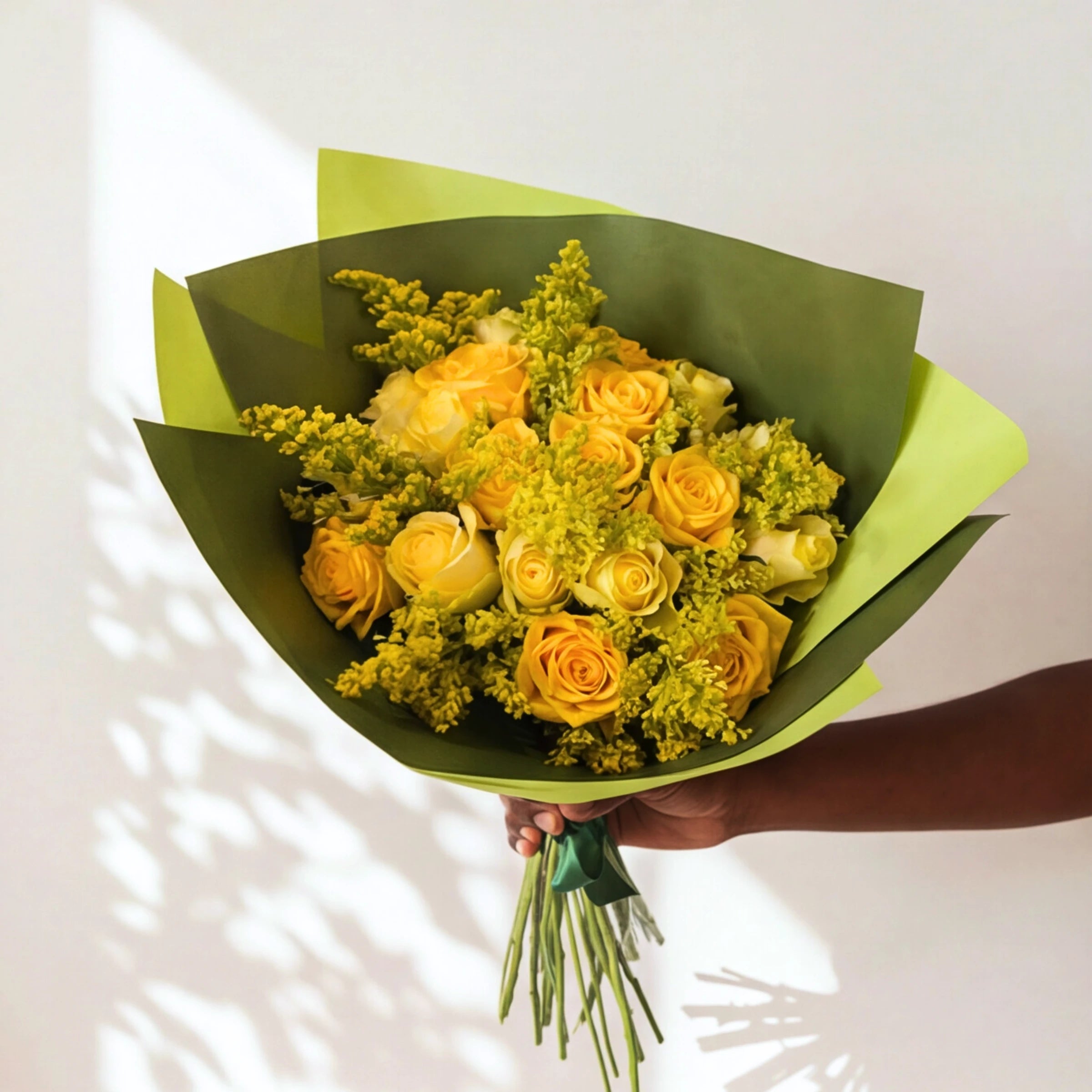 Meadowlark yellow flower bouquet of yellow roses and golden solidago in green wrap, held in soft light