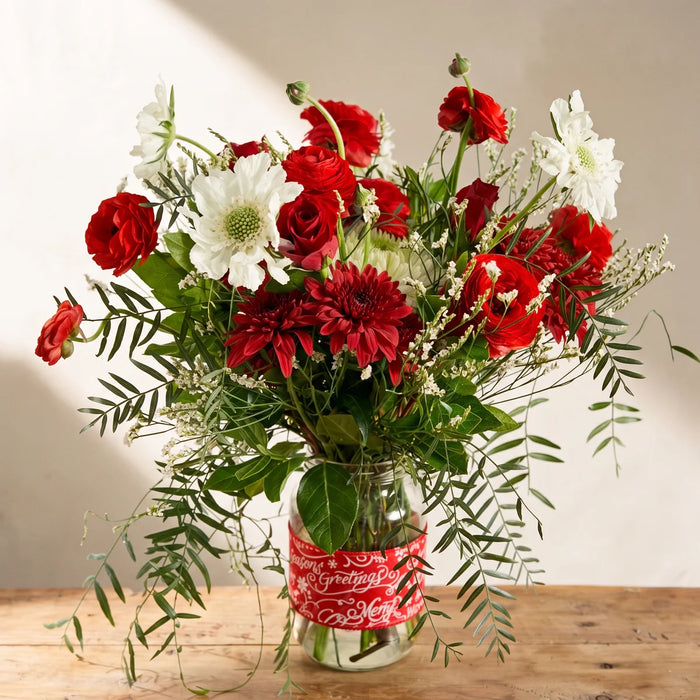 Red and white Christmas flowers in a glass jar with a red Season's Greetings band on a pine table, Fabulous Flowers South Africa