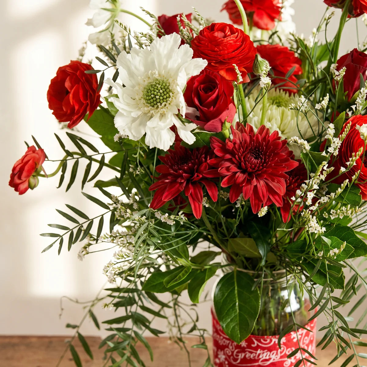 Close-up of red ranunculus, red chrysanthemums and a white scabiosa above a festive jar band, Fabulous Flowers South Africa