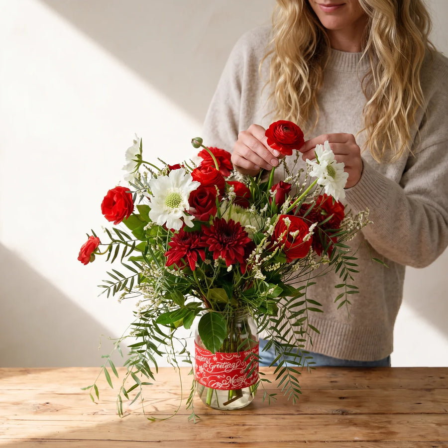 Woman in an oatmeal jumper adjusting a red ranunculus in a jar of Christmas flowers, Fabulous Flowers South Africa