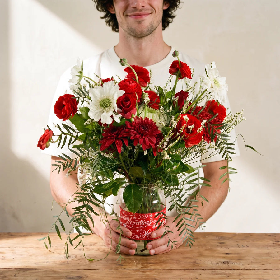 Man in a white t-shirt holding a jar of red and white Christmas flowers with trailing greenery, Fabulous Flowers South Africa