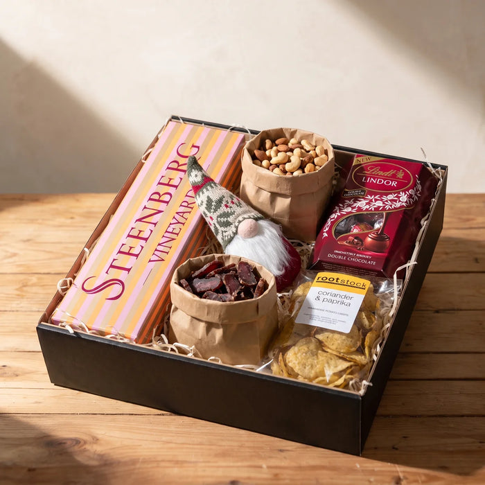 Open Christmas gift box with Steenberg MCC, Lindt Lindor, crisps and brown paper bags of nuts and biltong on a pine table, Fabulous Flowers South Africa