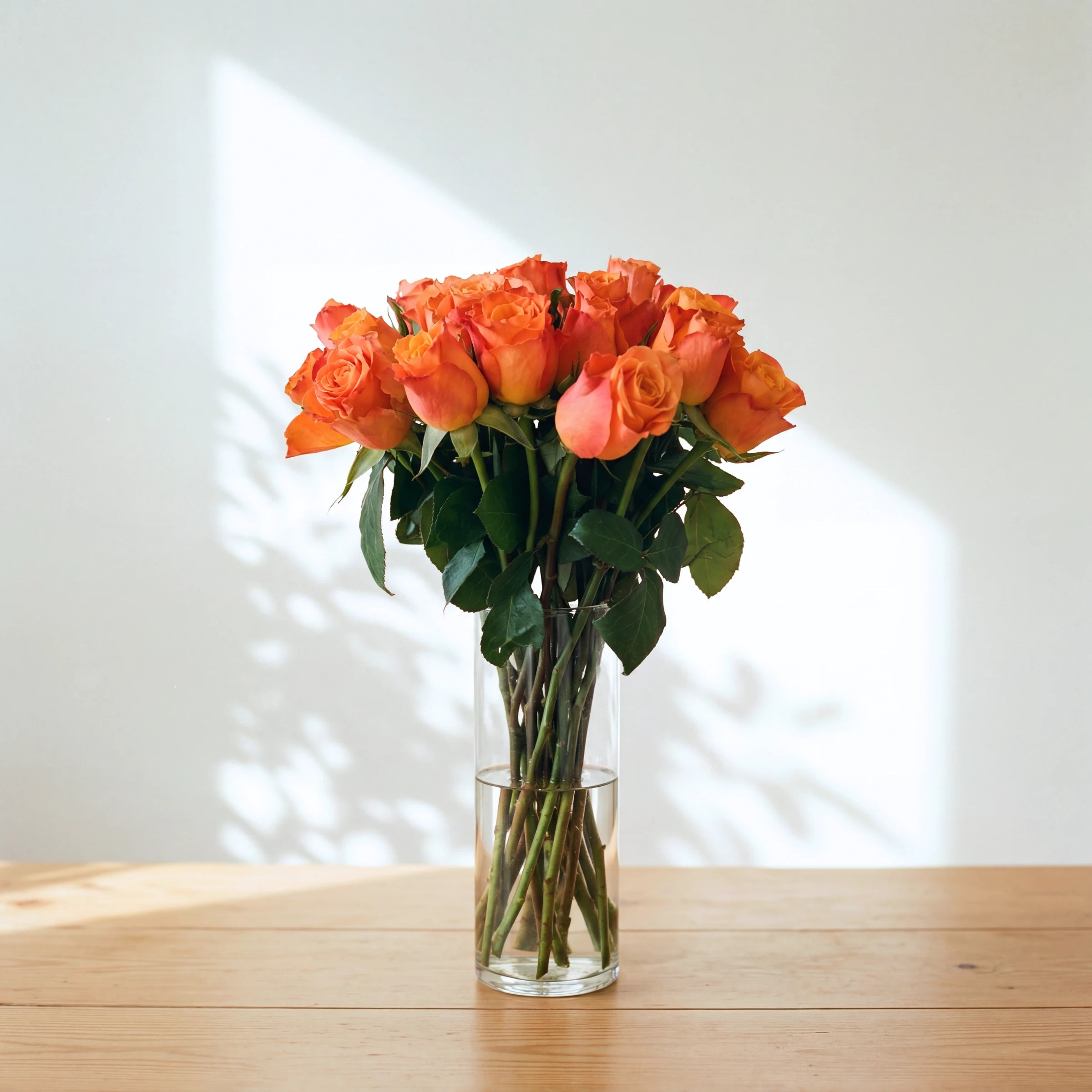 Mimosa orange roses in a vase, bright orange roses arranged in a clear glass cylinder vase on a wooden table