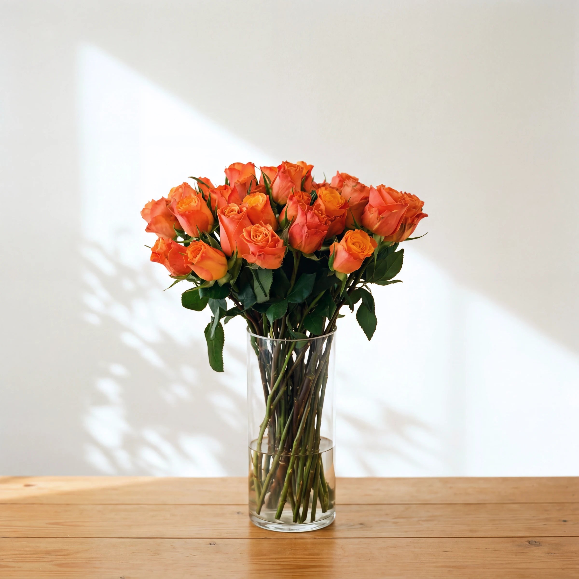 Mimosa orange rose arrangement, a fuller clear glass vase of bright orange roses in soft window light