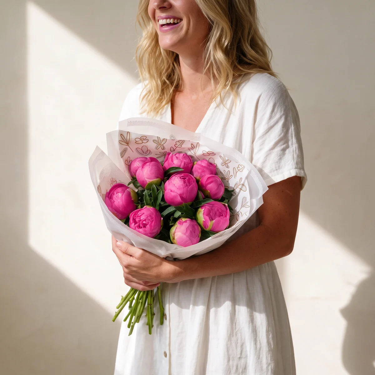 Blonde woman in a white dress laughing as she holds a bouquet of ten rose pink peonies at her waist, Fabulous Flowers South Africa
