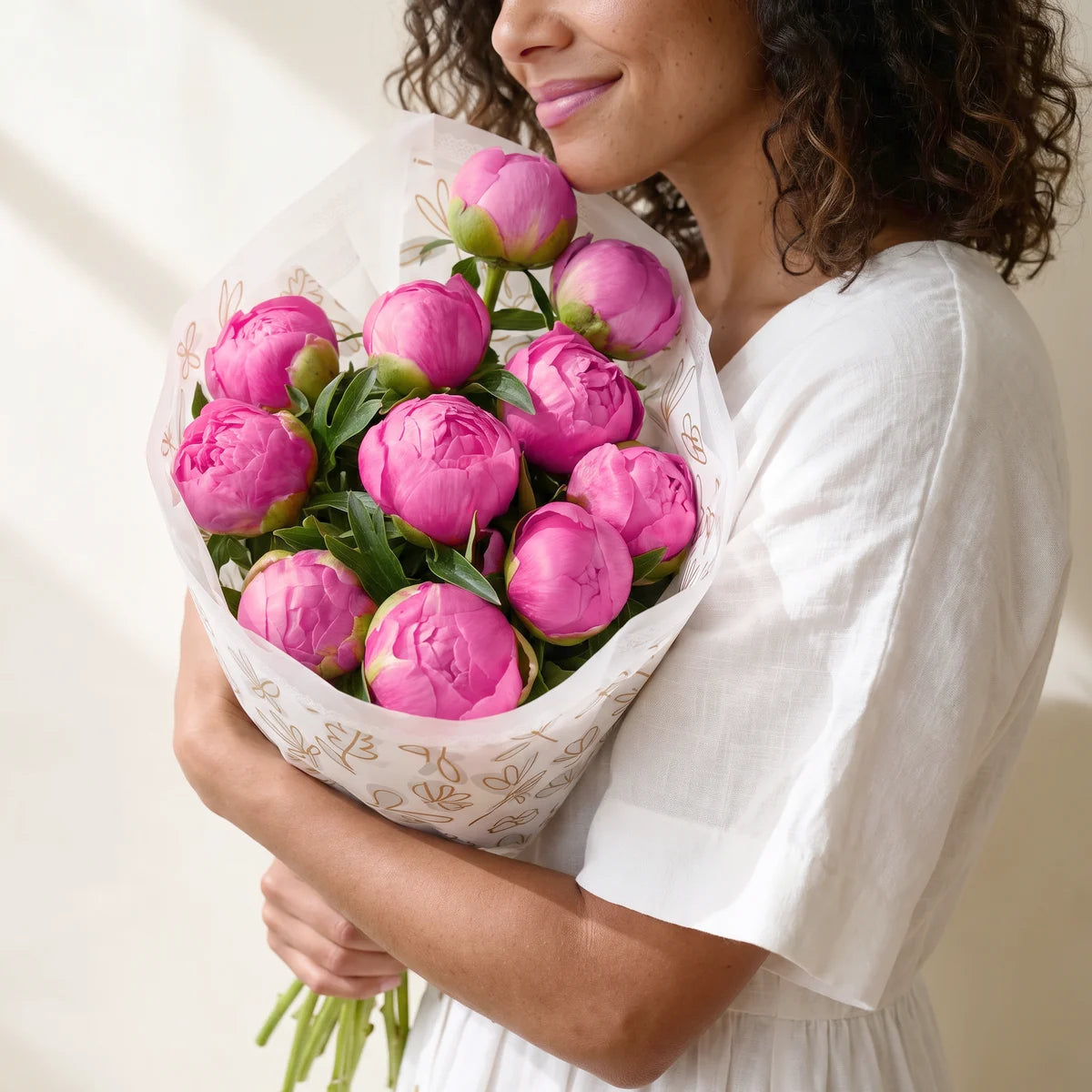 Woman with curly dark hair in a white dress hugging a large bouquet of pink peonies with her cheek resting against the blooms, Fabulous Flowers South Africa