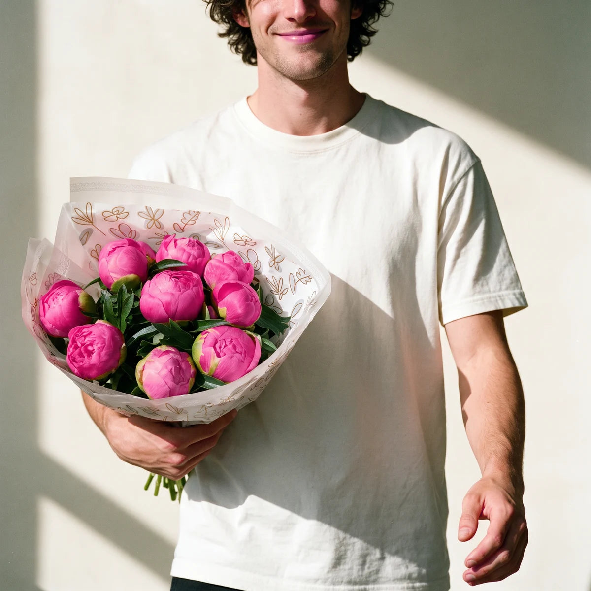 Smiling man with curly dark hair in a white t-shirt walking towards the camera carrying a large bouquet of twenty pink peonies, Fabulous Flowers South Africa