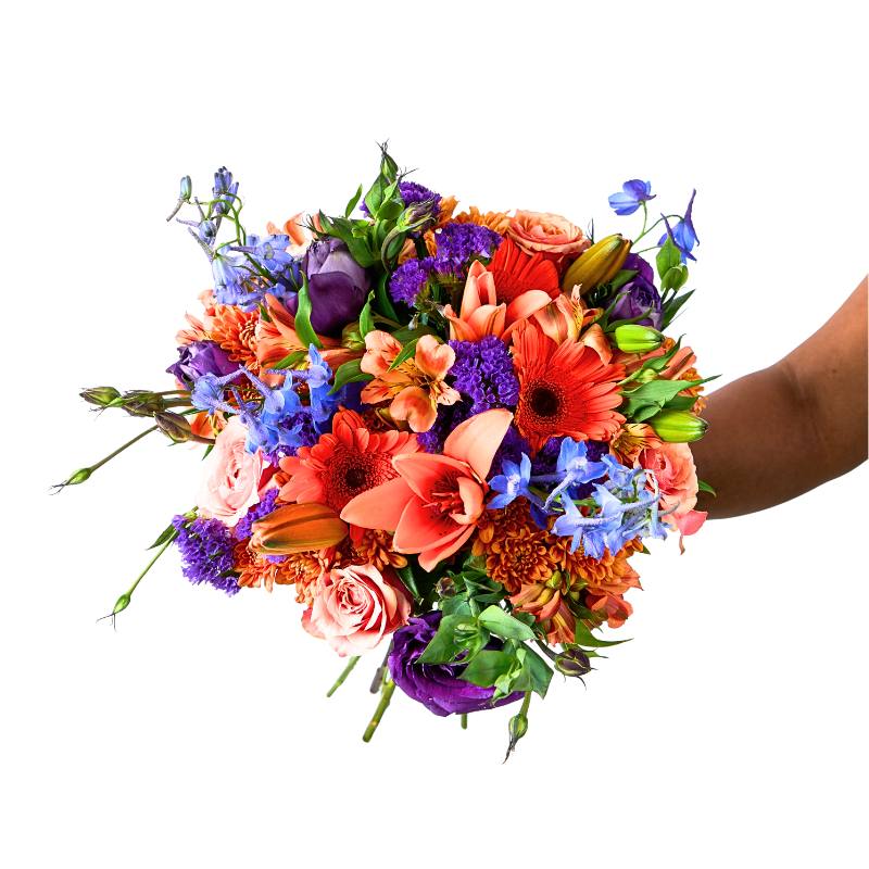 Mood Booster bouquet in hand — vibrant orange gerberas, peach roses, purple blooms and blue delphinium on a clean white background